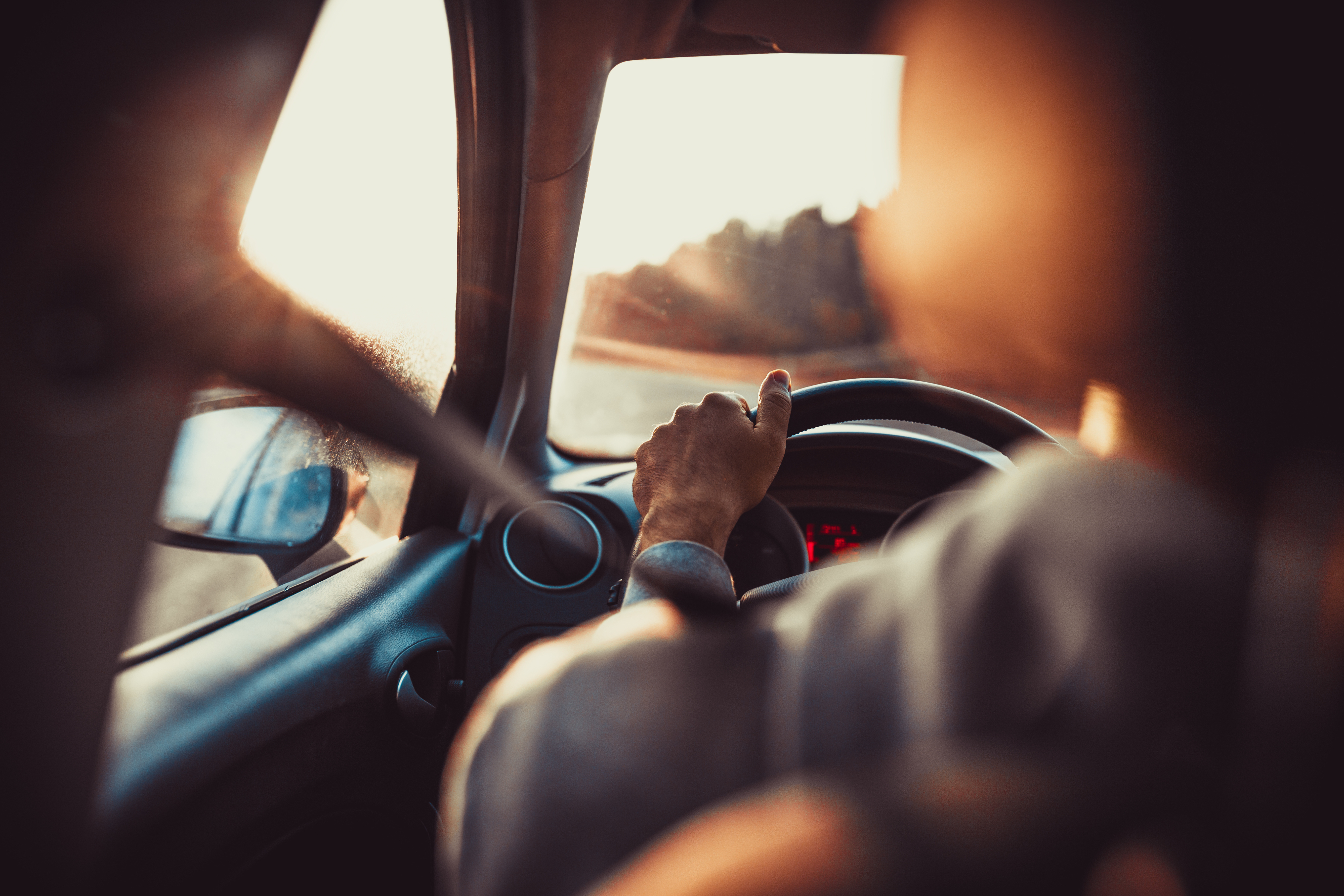 Driver with one hand on the steering wheel at sunset