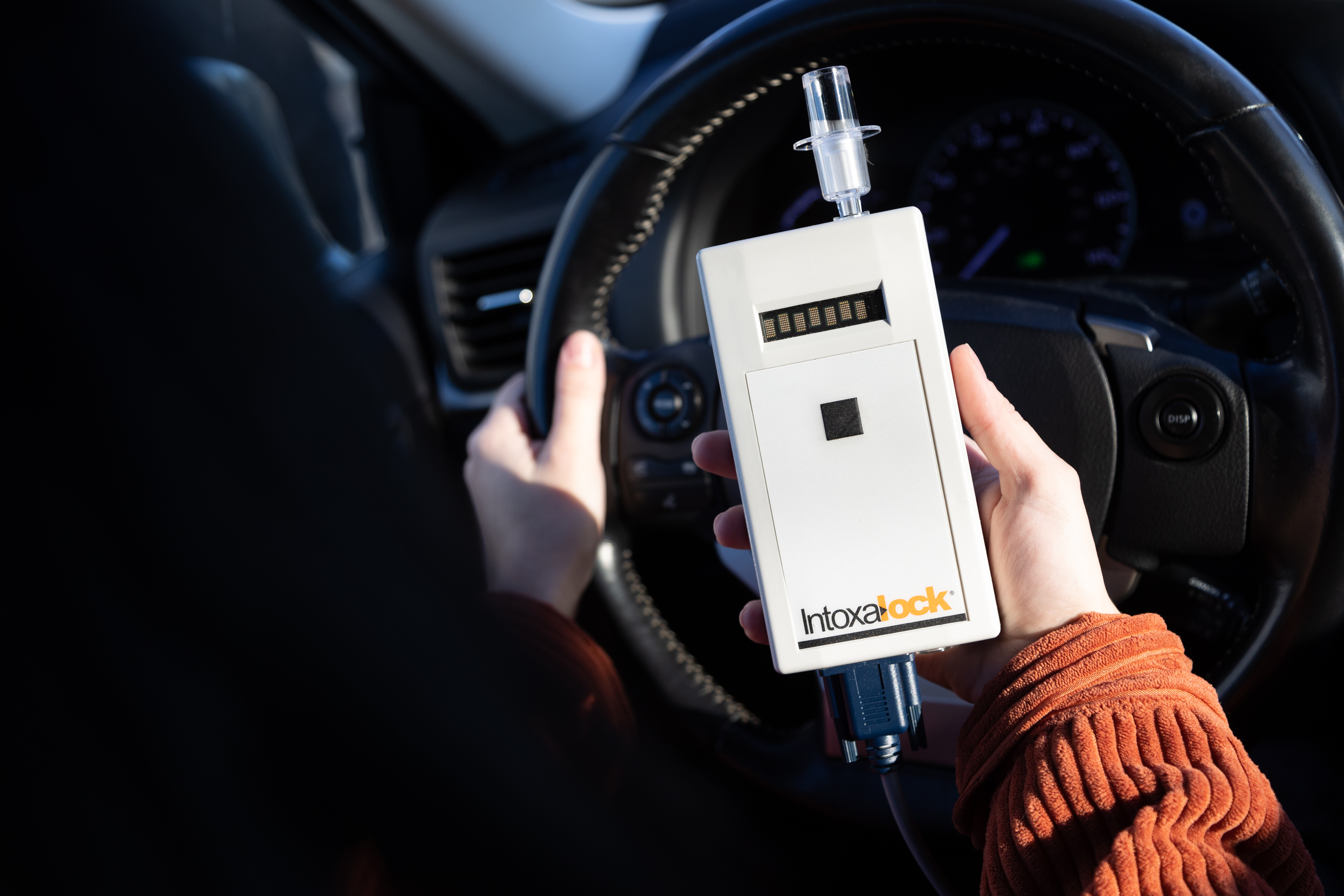 A closeup picture of a hand holding a Intoxalock breathalyzer device in a car. A closeup picture of a hand holding a Intoxalock breathalyzer device in a car.