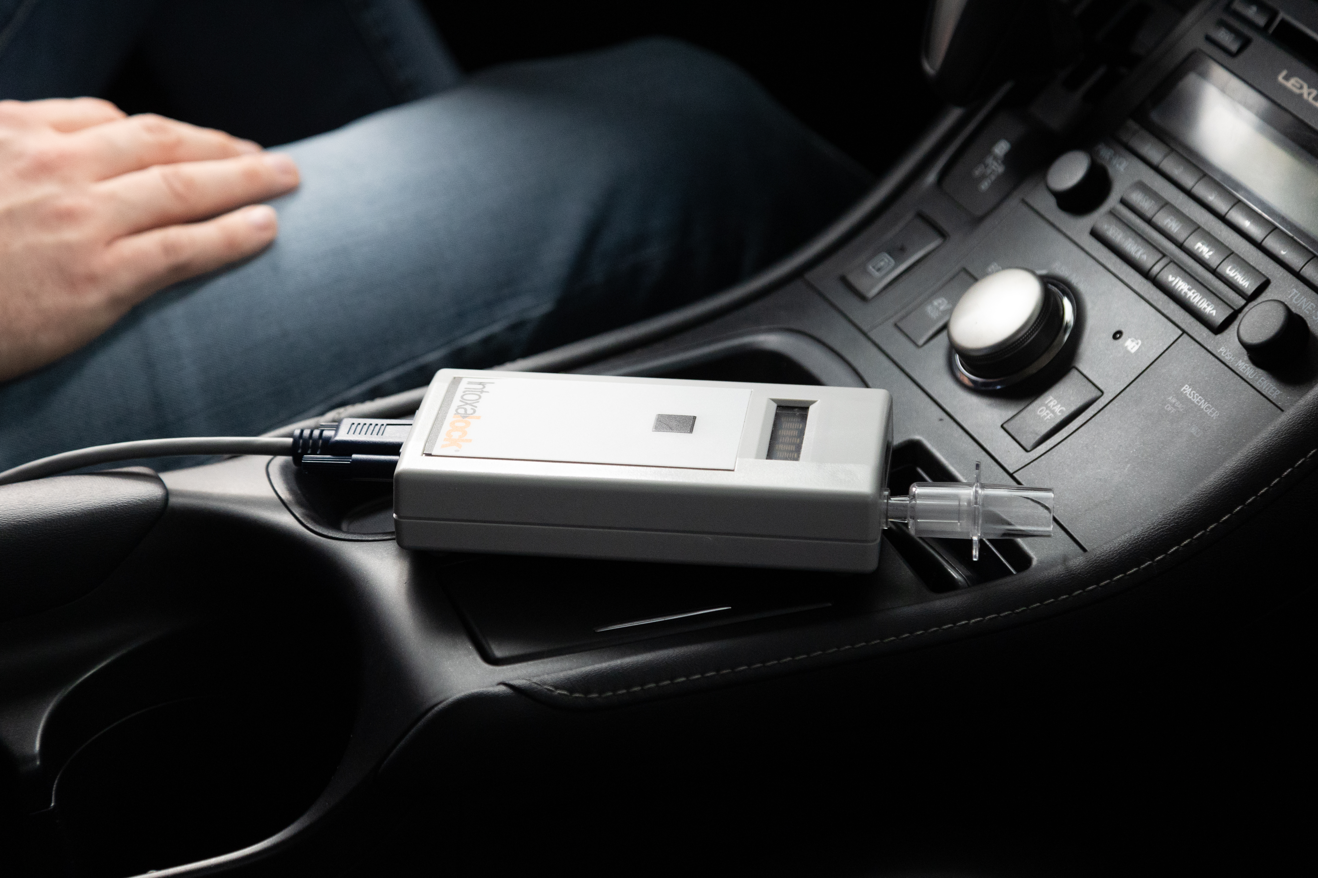 A closeup picture of a hand holding a Intoxalock breathalyzer device in a car. A closeup picture of a hand holding a Intoxalock breathalyzer device in a car.