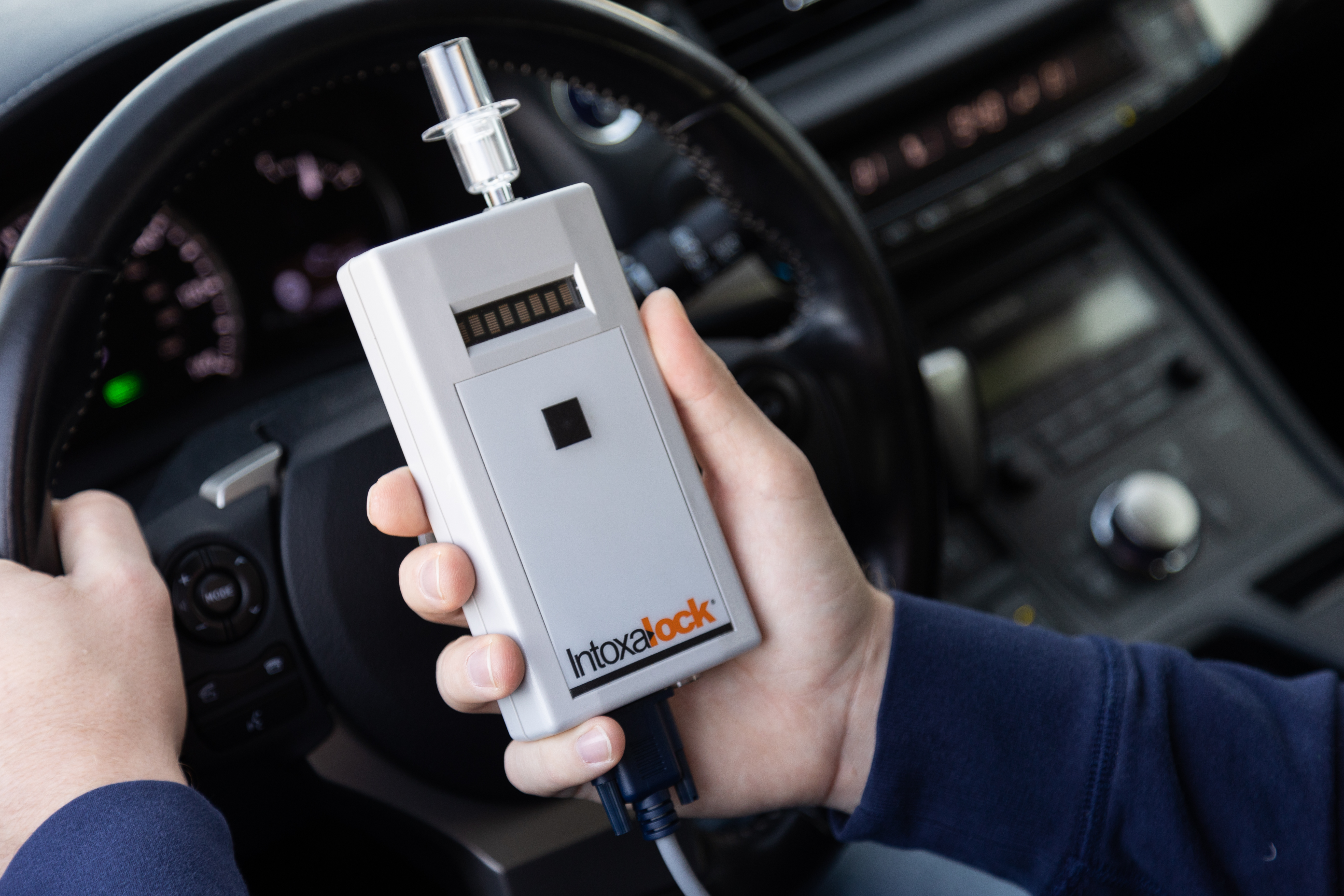 A closeup picture of a hand holding a Intoxalock breathalyzer device in a car. A closeup picture of a hand holding a Intoxalock breathalyzer device in a car.