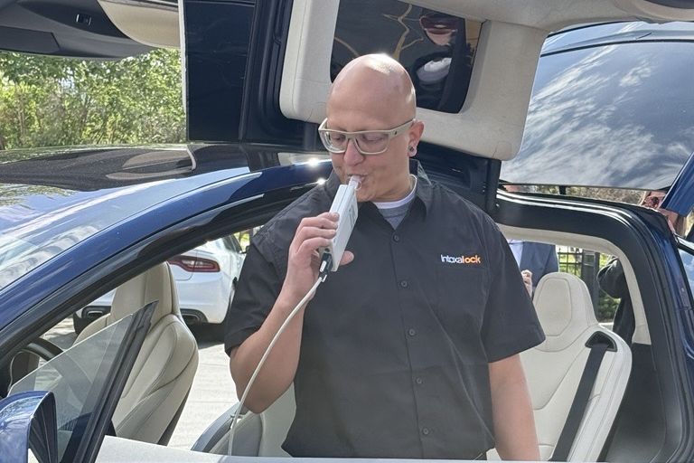 Ron Cardenas, Intoxalock Vehicle Installation Process Specialist, blowing into an ignition interlock handset inside an electric vehicle