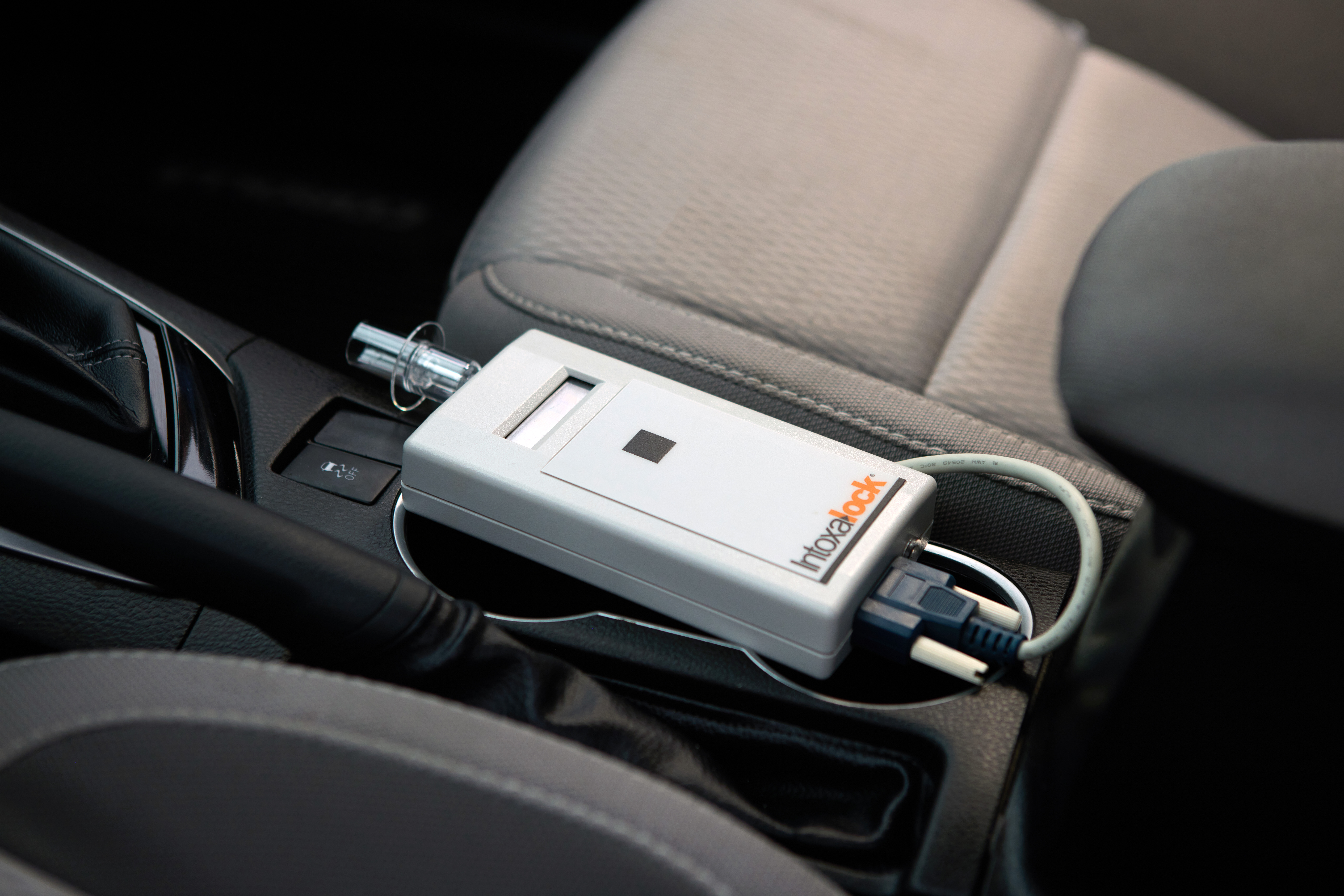 A closeup picture of a hand holding a Intoxalock breathalyzer device in a car. A closeup picture of a hand holding a Intoxalock breathalyzer device in a car.