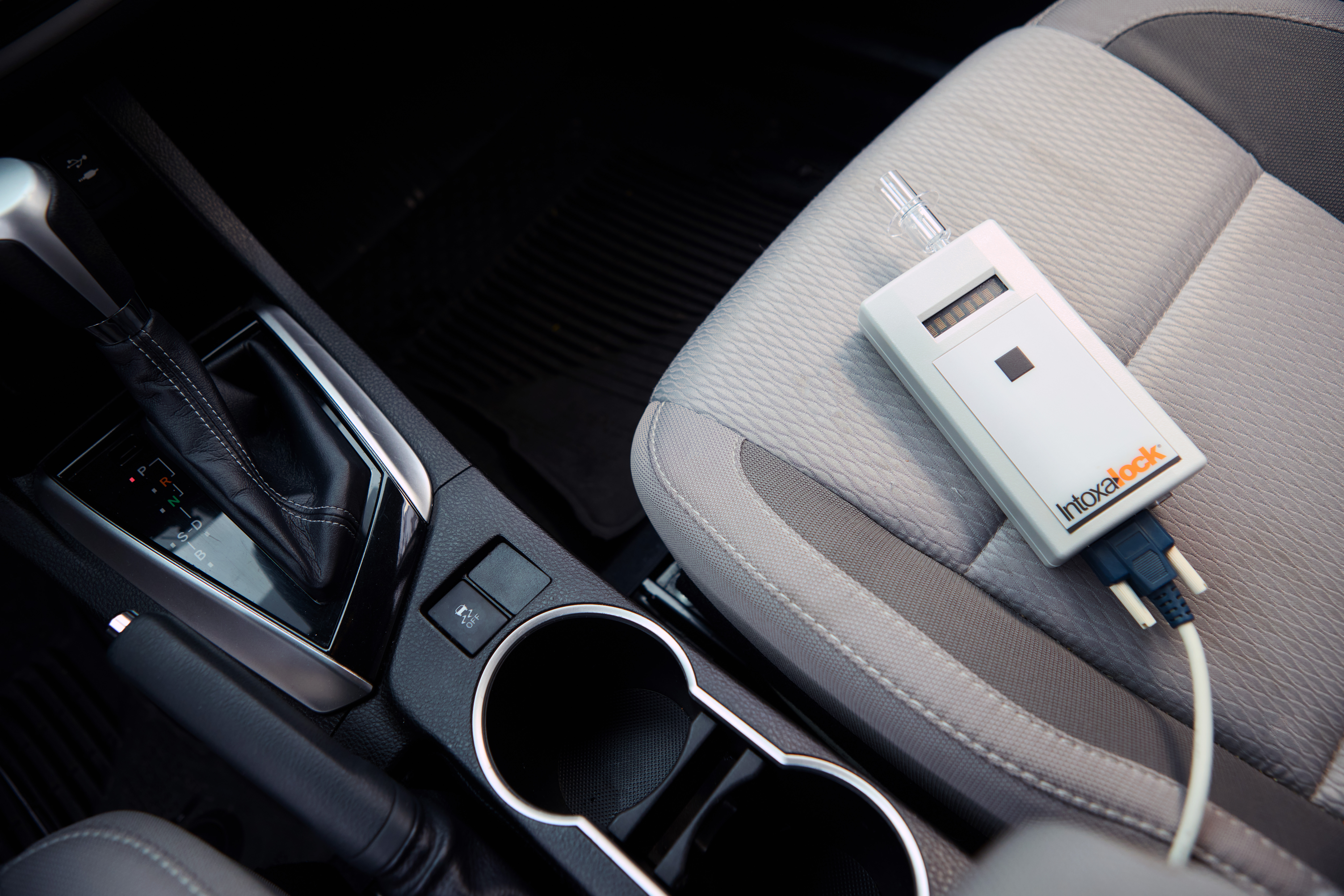 A closeup picture of a hand holding a Intoxalock breathalyzer device in a car. A closeup picture of a hand holding a Intoxalock breathalyzer device in a car.