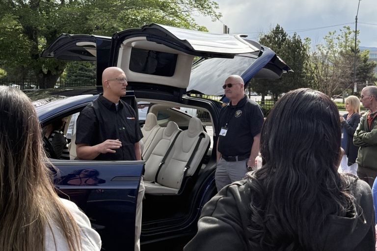 Ron Cardenas speaking to a group beside a Tesla Model X with its falcon-wing doors open
