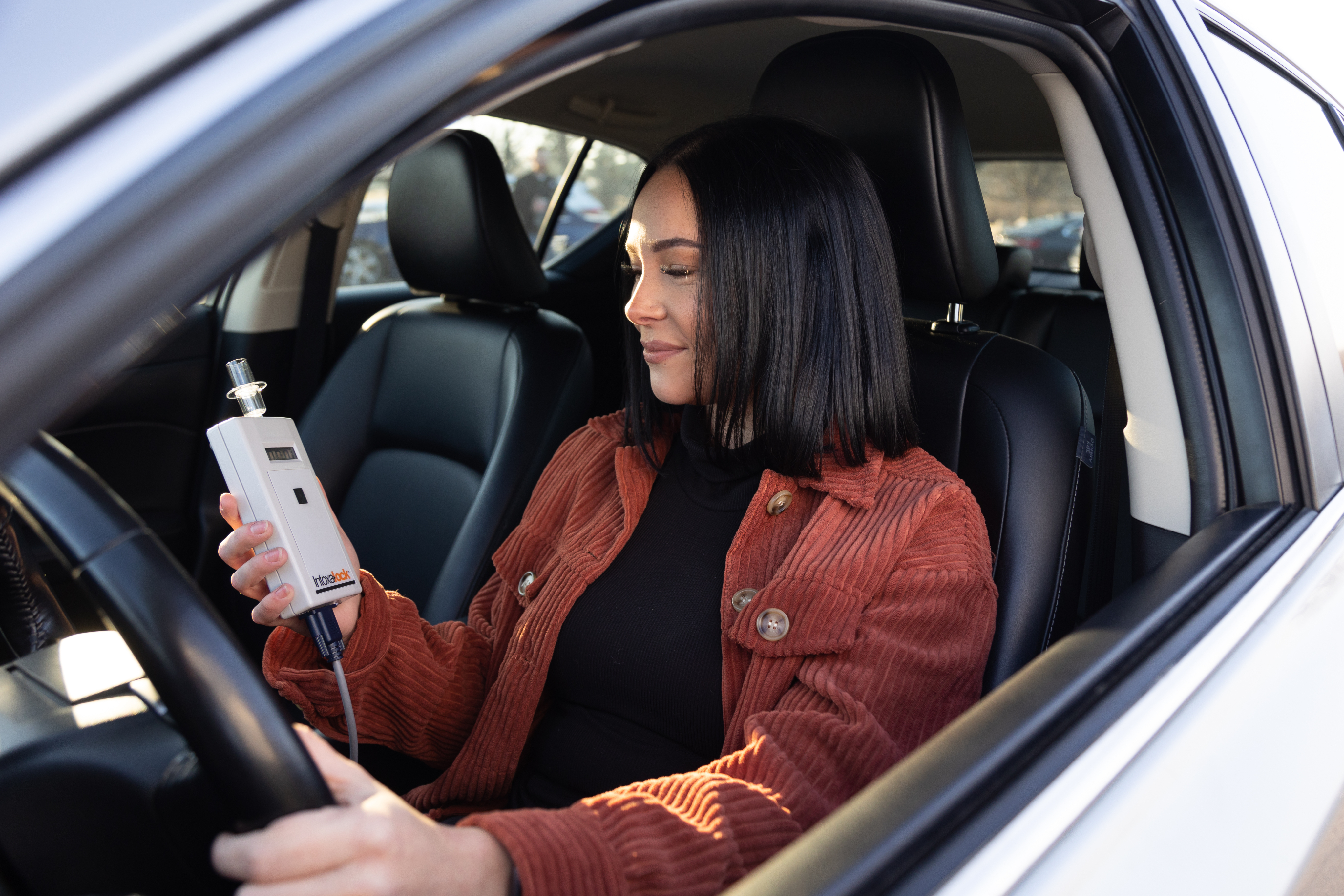 Woman seated in her car holding an Intoxalock ignition interlock device