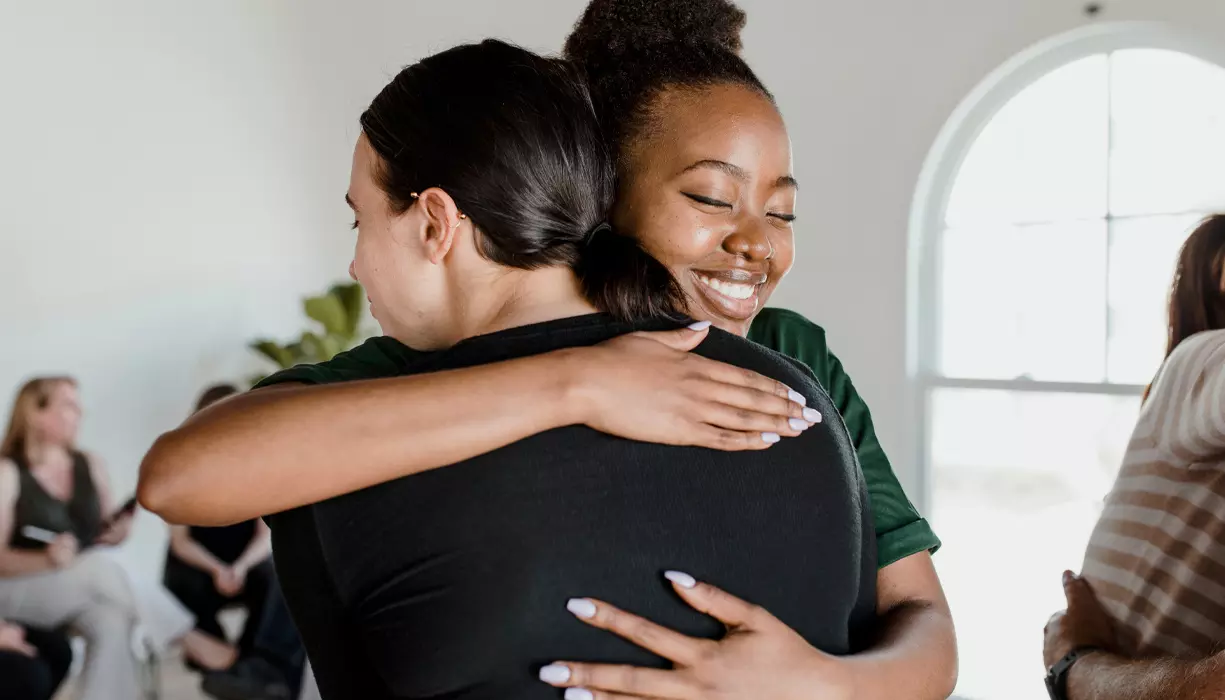 Picture of two women hugging in a bright room.
