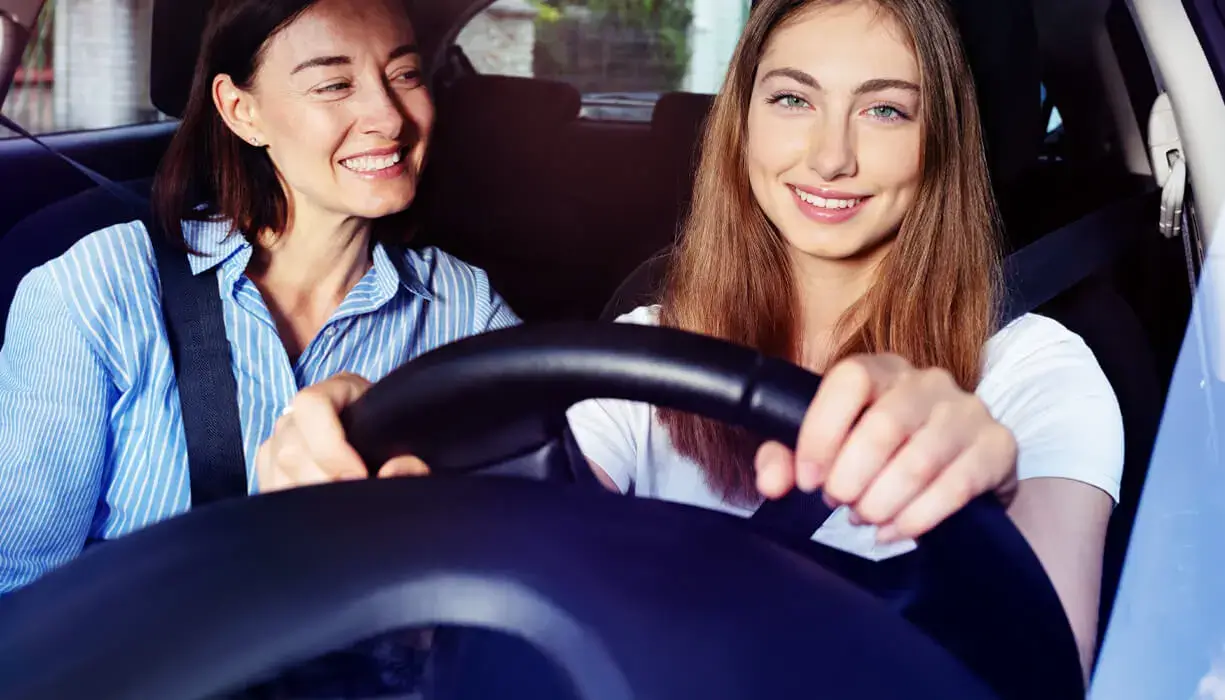 Mother encouraging her teenage daughter who is smiling while driving, illustrating parental support in regaining a driver's license after a DUI