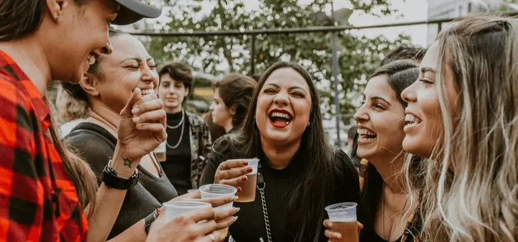 Group of underage girls laughing and holding alcoholic drinks at an outdoor party