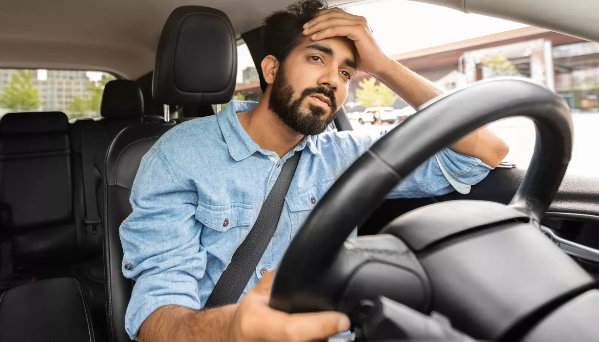 Man sitting in a car looking concerned about something.