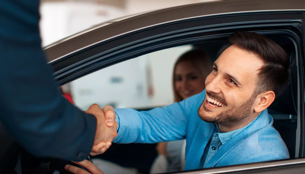 A man shaking hand with another person through a car window.