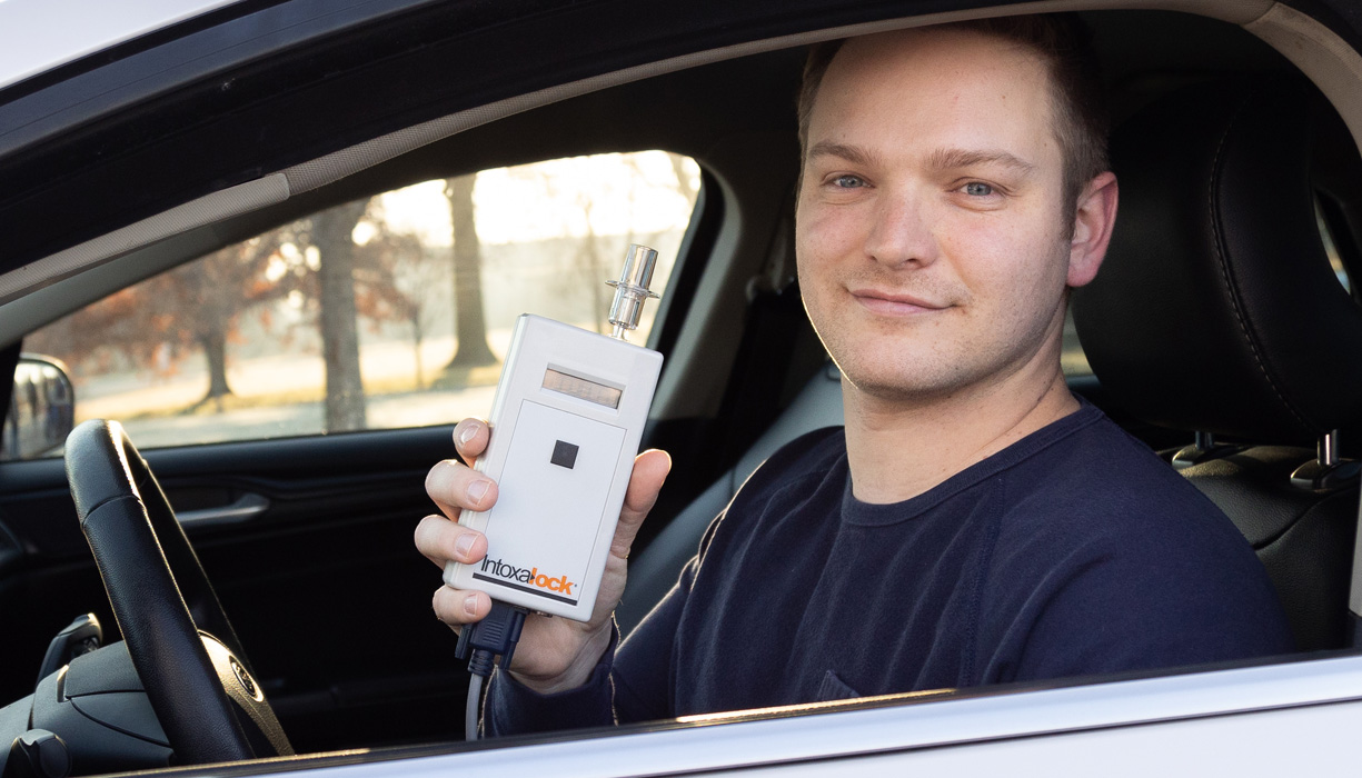 A man holding an Intoxalock ignition interlock device, which is installed in their vehicle to measure breath alcohol concentration before the vehicle can start.