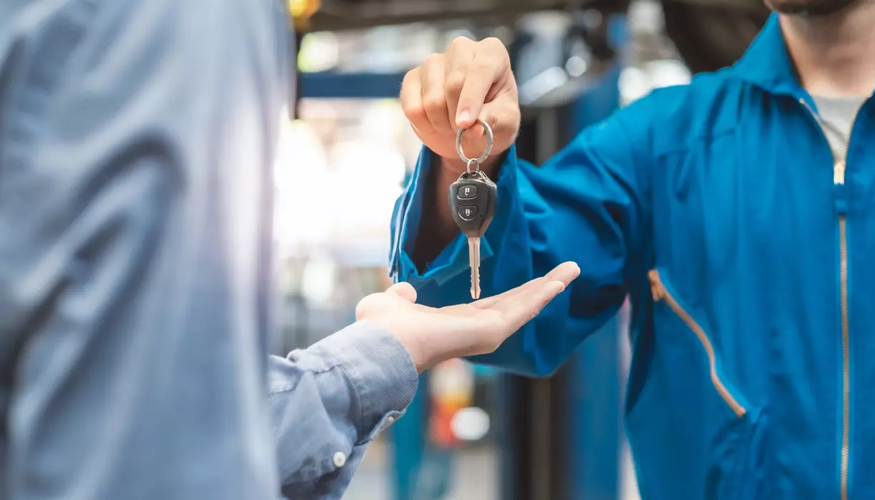 A person handing set of car keys to another person through a car window.