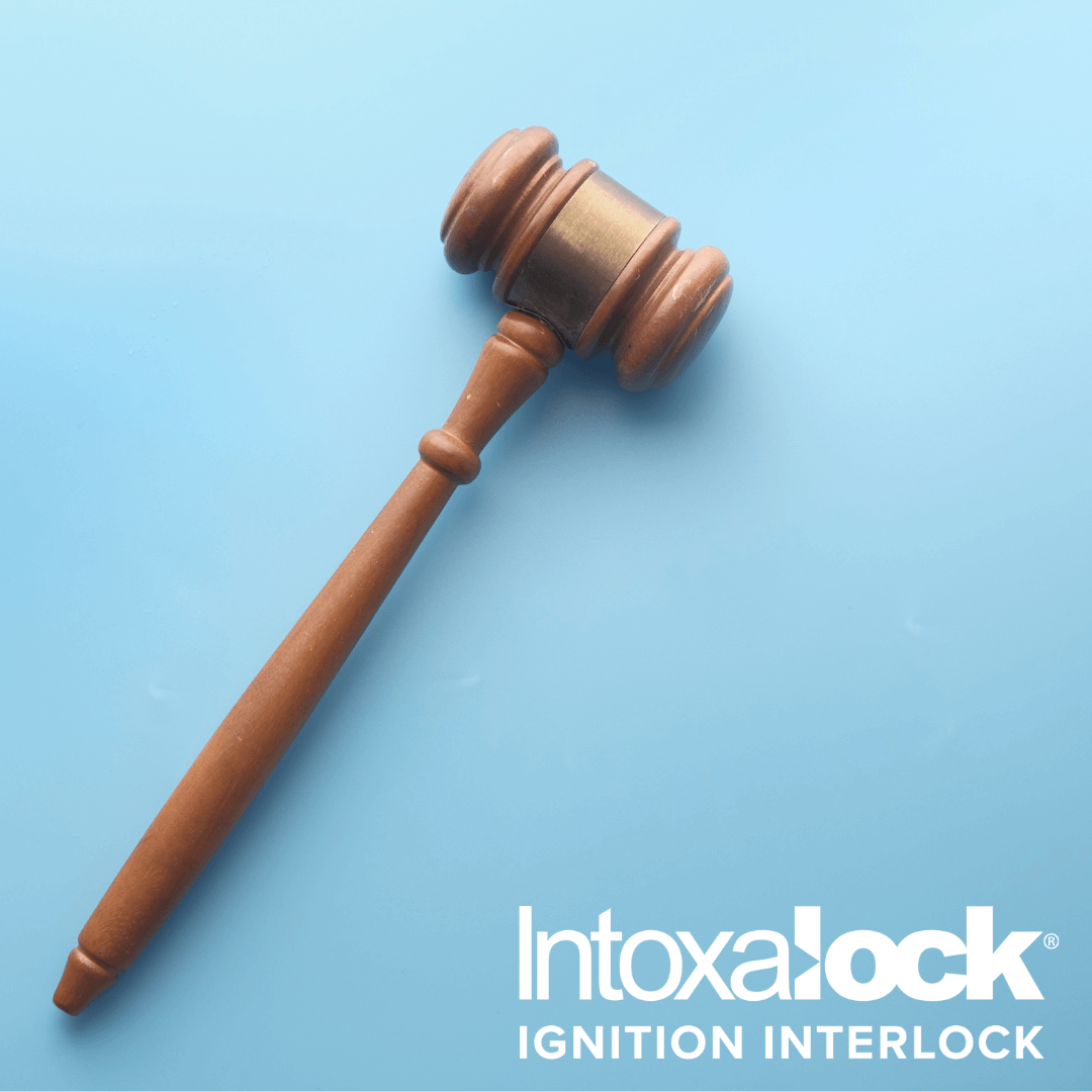A wooden gavel lays in a slanted position against a pale blue background. The Intoxalock ignition interlock device logo is in white text in the bottom right corner.