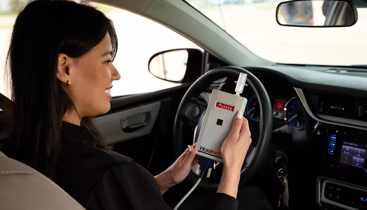 A woman sitting in a car holding a ignition interlock device.