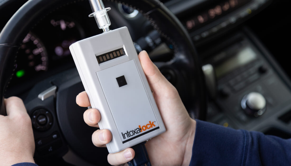 A man holding an Intoxalock ignition interlock device, which is installed in their vehicle to measure breath alcohol concentration before the vehicle can start.