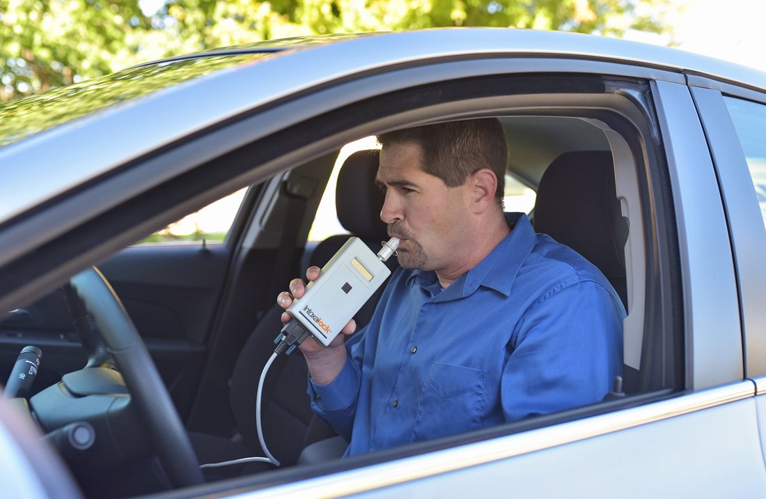 A man blowing into an Intoxalock ignition interlock device, which is installed in their vehicle to measure breath alcohol concentration before the vehicle can start.