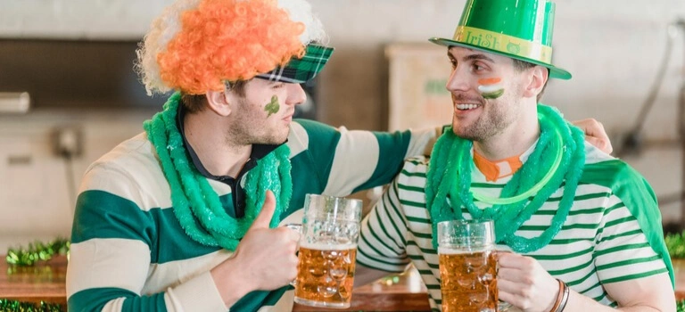 Two friends in green outfits celebrating St. Patrick’s Day and clinking beer mugs