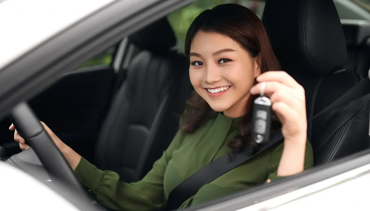 Smiling woman sitting in the driver's seat of a car, holding up a set of car keys