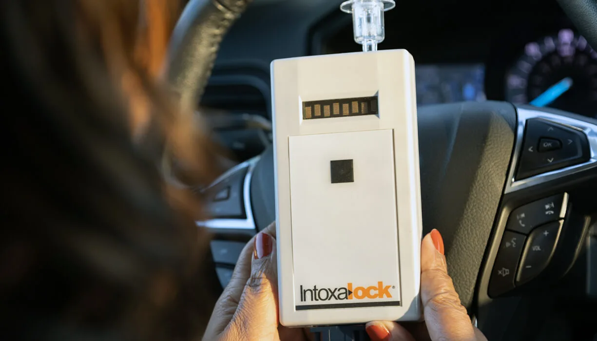 A person holding an Intoxalock ignition interlock device, which is installed in their vehicle to measure breath alcohol concentration before the vehicle can start.