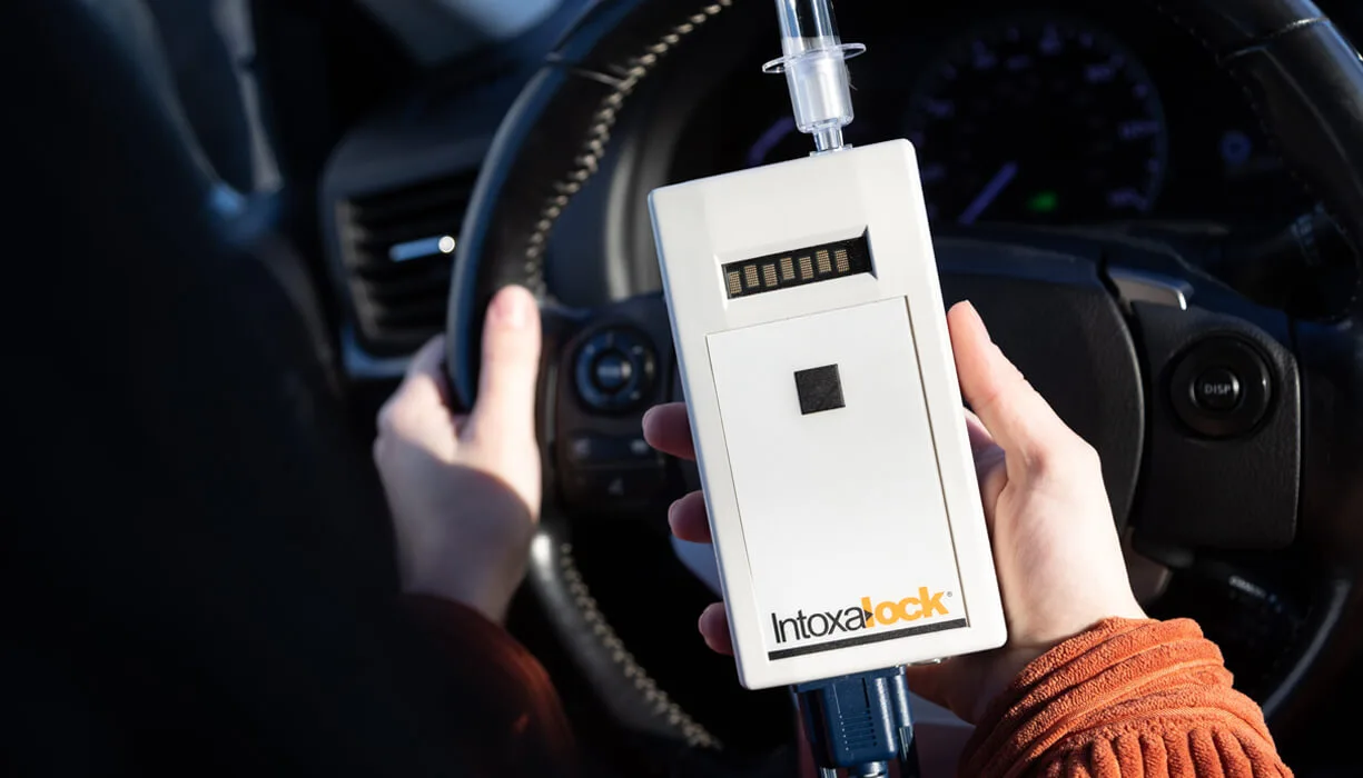 Close-up of an Intoxalock ignition interlock device held by a person inside a car, illustrating the device's design and functionality.