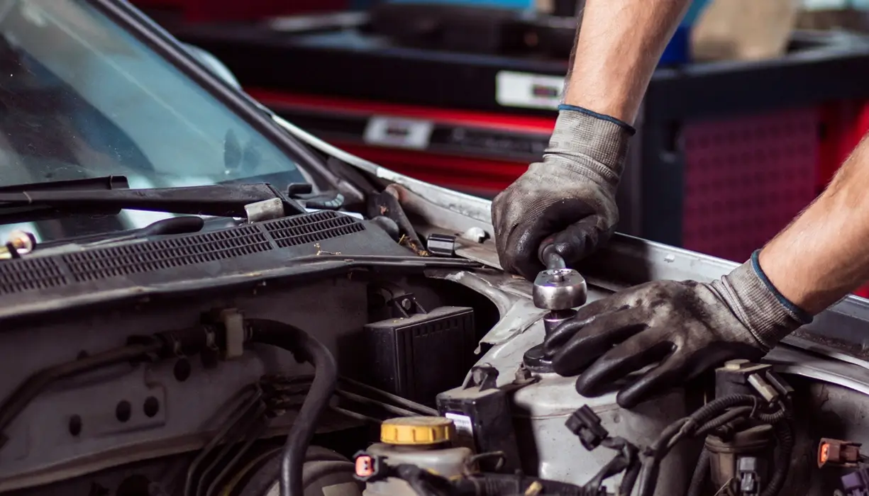 A service mechanic wearing gloves is working on a car.